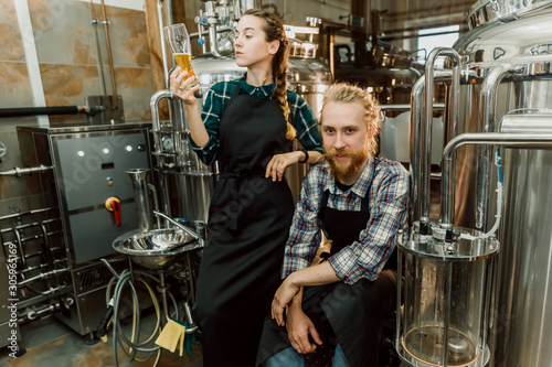 Brewery workers looking at freshly made beer in glass tube and discussing it. Male and female brewer testing beer at brewery factory. 4k. Small business concept.