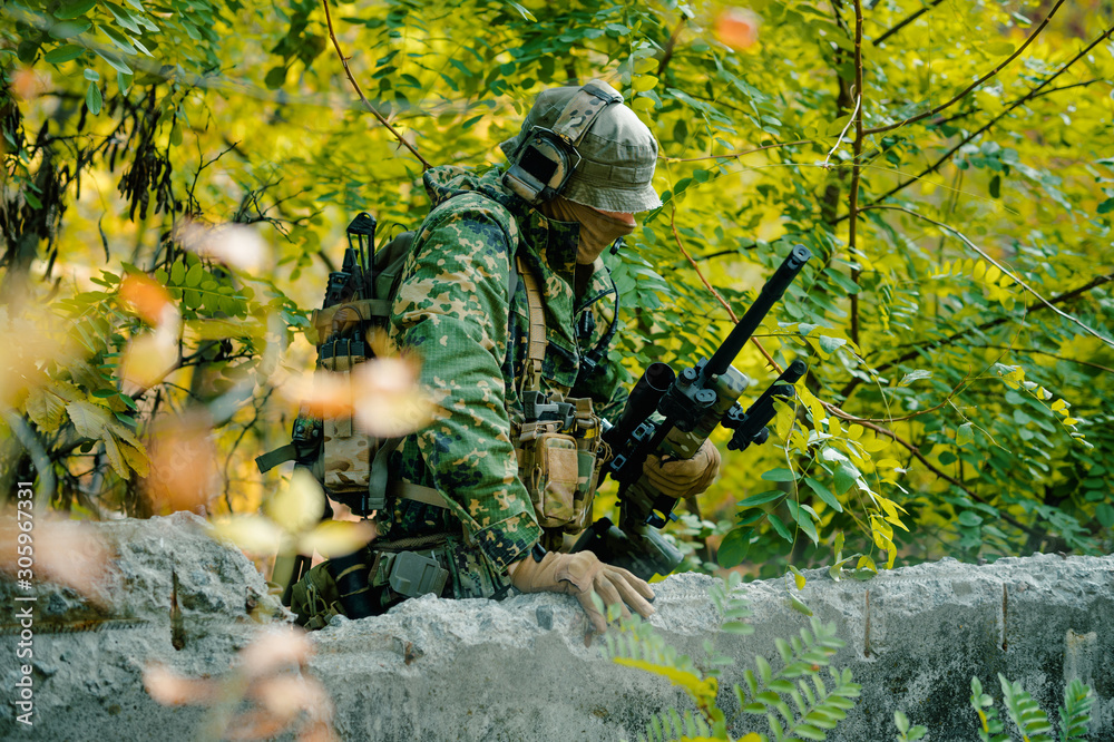 Man in uniform, behind the wall with sniper rifle on green forest background Man in uniform, behind the wall with sniper rifle on green forest background