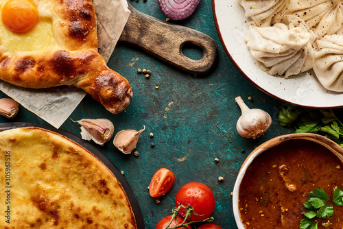 top view of delicious khinkali, Adjarian and imeretian khachapuri, kharcho on green background photo