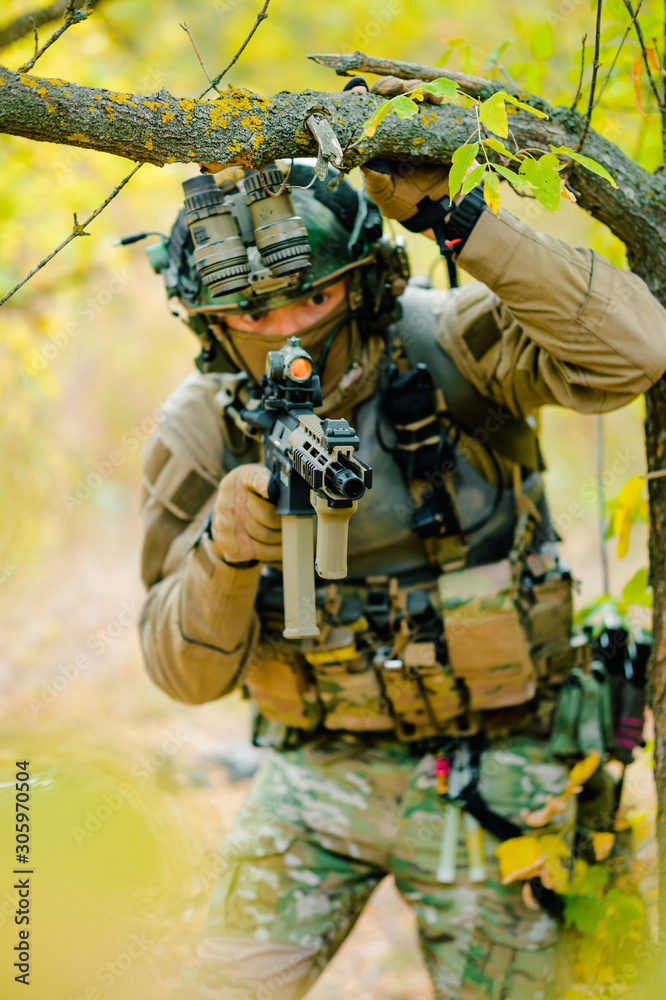 Closeup airsoft man in uniform with machine gun move through the forest. Soldier aims at the sight. Vertical photo Closeup airsoft man in uniform with machine gun move through the forest. Soldier aims at the sight. Vertical photo