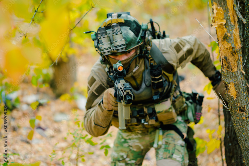 Airsoft man in uniform with machine gun move through the forest. Soldier aims at the sight