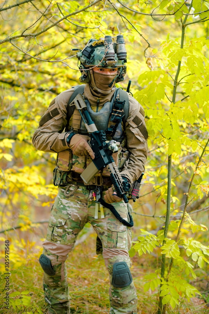 Airsoft man in uniform with machine gun standing on yellow forest backdrop. Vertical photo