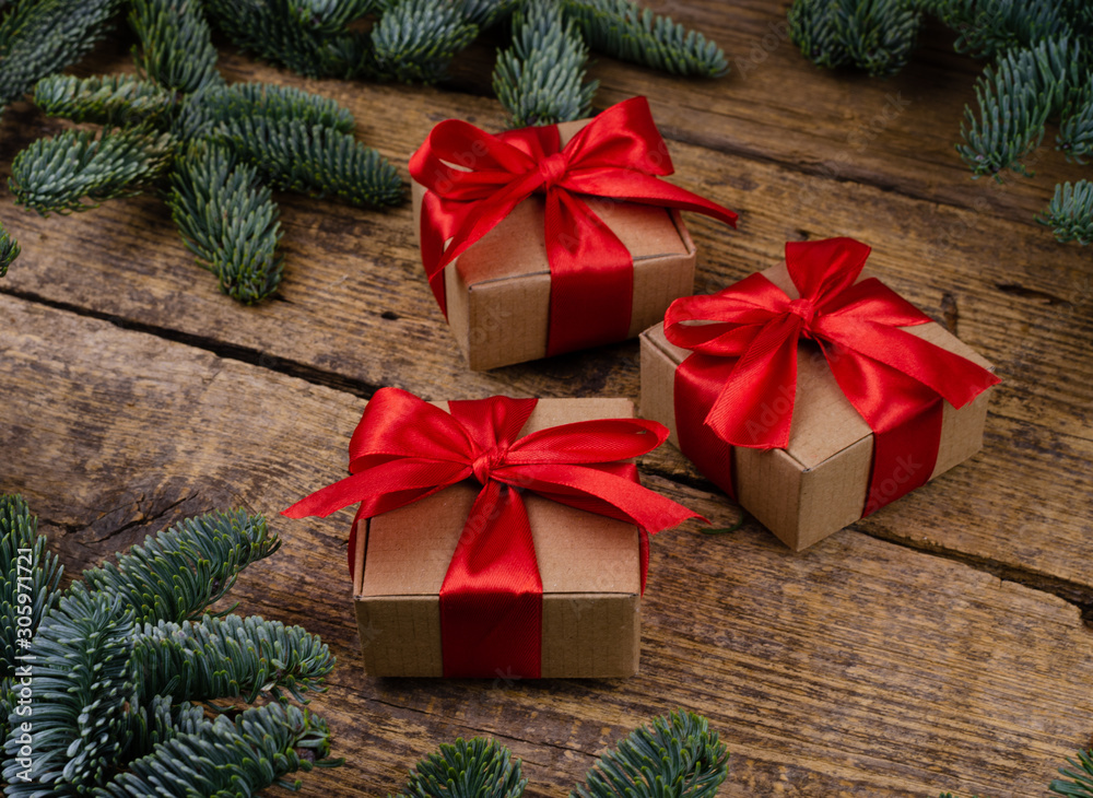 Side view of three brown paper boxes with bright red ribbons on a wooden background with green Christmas tree branches.