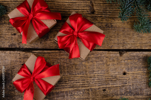 Close view of three brown cardboard boxes with red bows on a wooden background with live Christmas tree branches.
