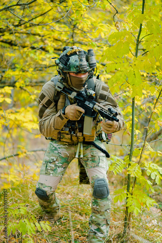 Airsoft man in uniform  move with machine gun on yellow forest backdrop. Vertical photo