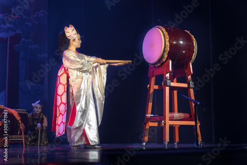 Traditional Japanese performance. Actress in white traditional japanese stage costume komono and fox mask hits the big taiko drum. photo