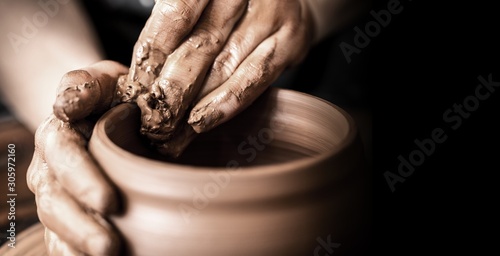 Hands of potter making clay pot on black background