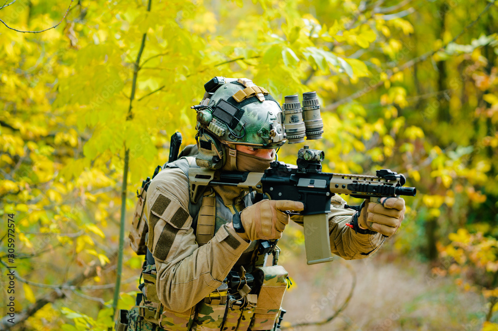 Airsoft man in uniform, stand with machine gun on yellow forest backdrop. Soldier aims at the sight Airsoft man in uniform, stand with machine gun on yellow forest backdrop. Soldier aims at the sight