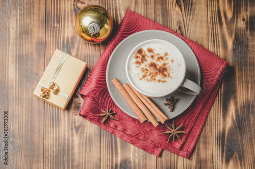Eggnog. Traditional christmas cocktail, cinnamon sticks on a red napkin and with decorations gift box and christmas toy. Wooden background. Top view.