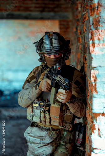 Man in uniform with machine gun and night-vision device stand beside broken wall. Airsoft soldier in night building. Vertcal photo