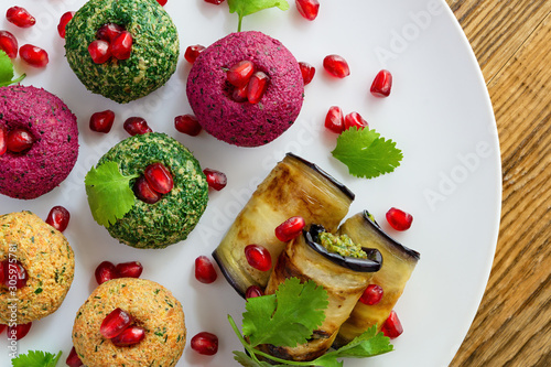 pkhali and badrijani  decorated with pomegranate seeds and coriander leafs on white plate placed on wooden background