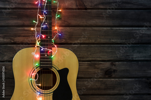 Acoustic guitar in a New Year's garland, guitar in a garland under a wooden wall, copy spaсe 