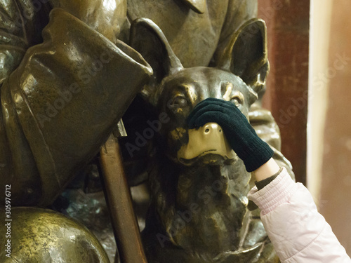 Girl touching the nose of dog statue in the Moscow subway station. Detail of statue of a red guarder with a dog . photo