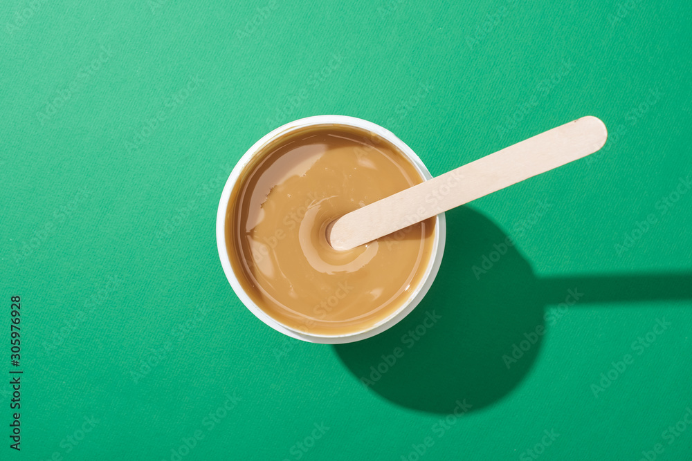 top view of depilation wax in cup with stick on green background top view of depilation wax in cup with stick on green background