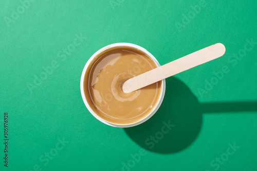 top view of depilation wax in cup with stick on green background