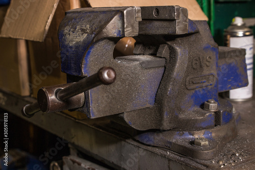 Dirty grimy industrial grip vice for holding heavy objects whilst working on them. Attached to wrack bench also full of debris of metal and wood shavings, blue object covered in black dirt and grime.