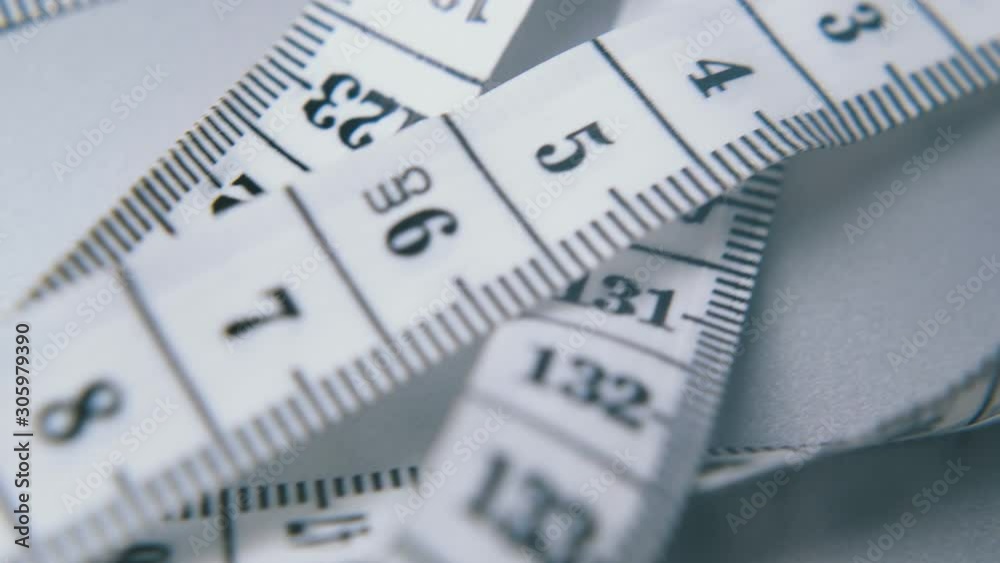 long white soft plastic measuring tape with calibrated in centimeters lies on light grey surface extreme close view long white soft plastic measuring tape with calibrated in centimeters lies on light grey surface extreme close view