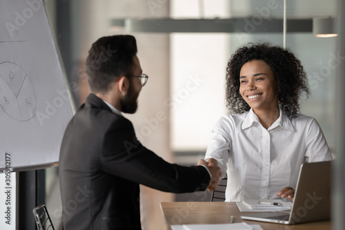 Smiling biracial businesswoman handshake male colleague at briefing