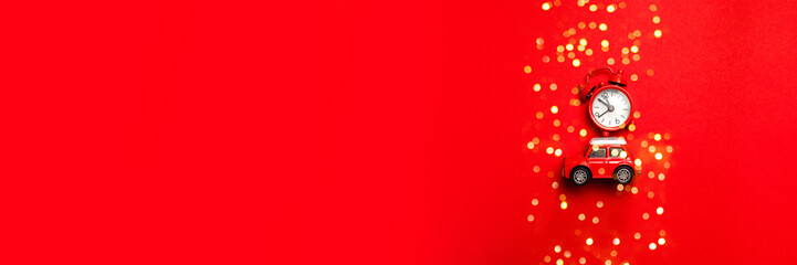 Little red toy car and red clock on a red background. Minimal design for celebrating 2024 Christmas or new year greeting card. Time to celebrate