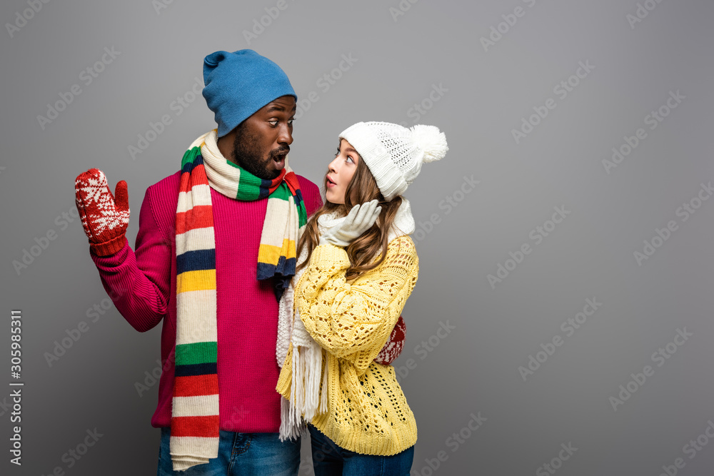 smiling interracial couple in winter outfit hugging on grey background
