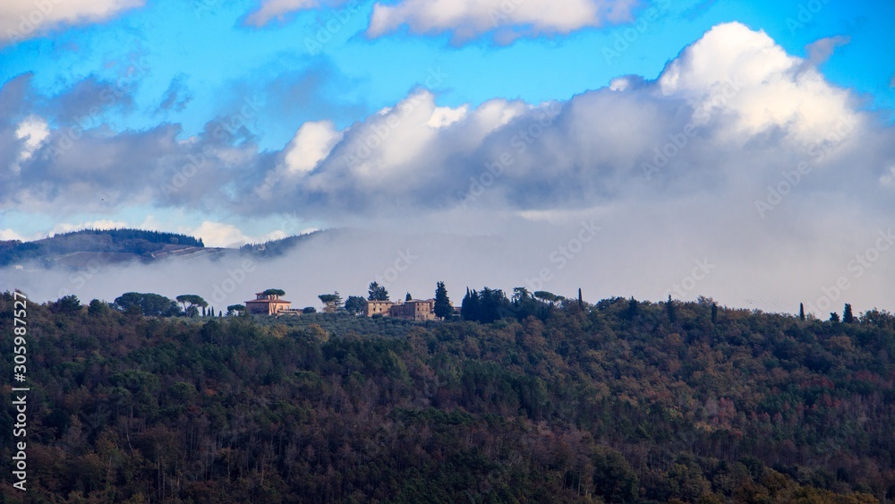 Fototapeta premium Italian pintoresque village in the mountains with fog under cloudy and blue sky