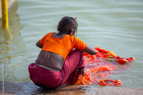 Foto Life on the Ganges: Low caste untouchable indian woman washing a bright orange sari in t he holy river Ganges
