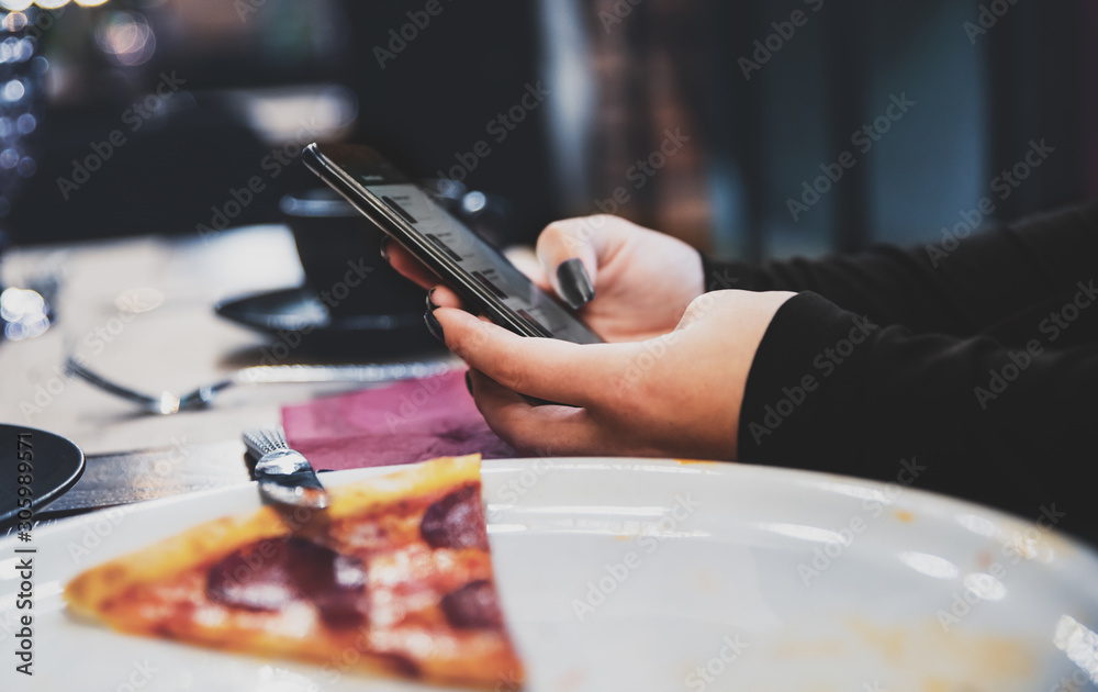 Fototapeta premium woman hand using mobile phone in cafe with a piece of pizza in plate on table