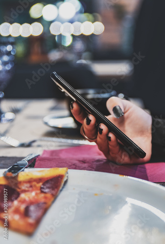 woman hand using mobile phone in cafe with a piece of pizza in plate on table