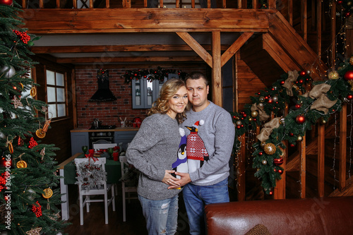 pregnant wife with husband posing next to a Christmas tree