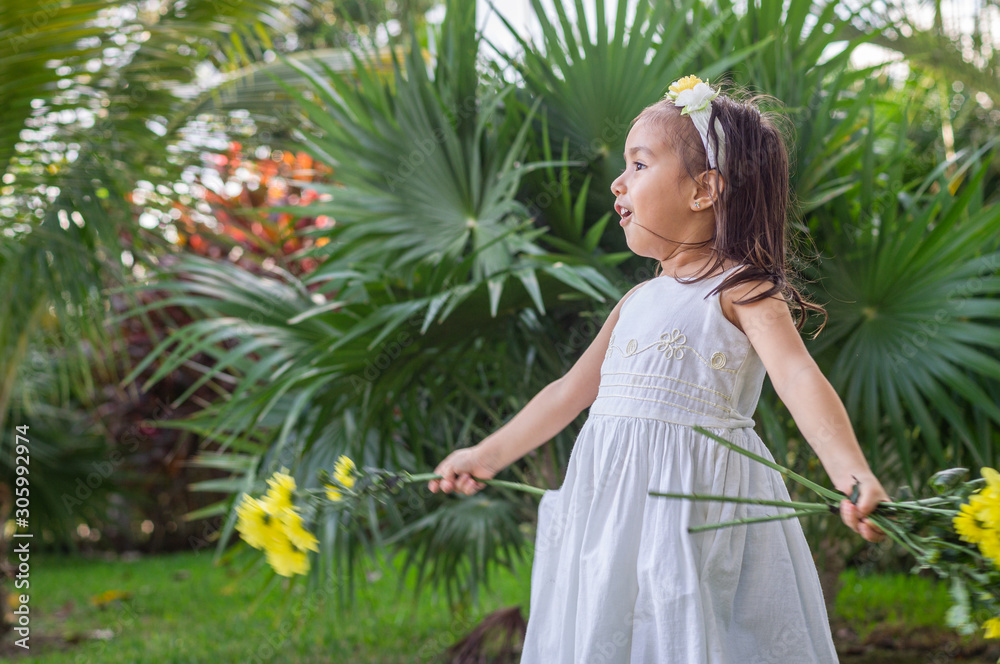 A girl in the garden with headband, white dress and branches of yellow natural flowers in her hands, sings