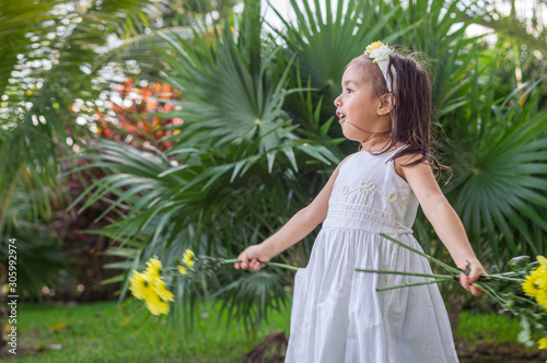 A girl in the garden with headband, white dress and branches of yellow natural flowers in her hands, sings © Luis