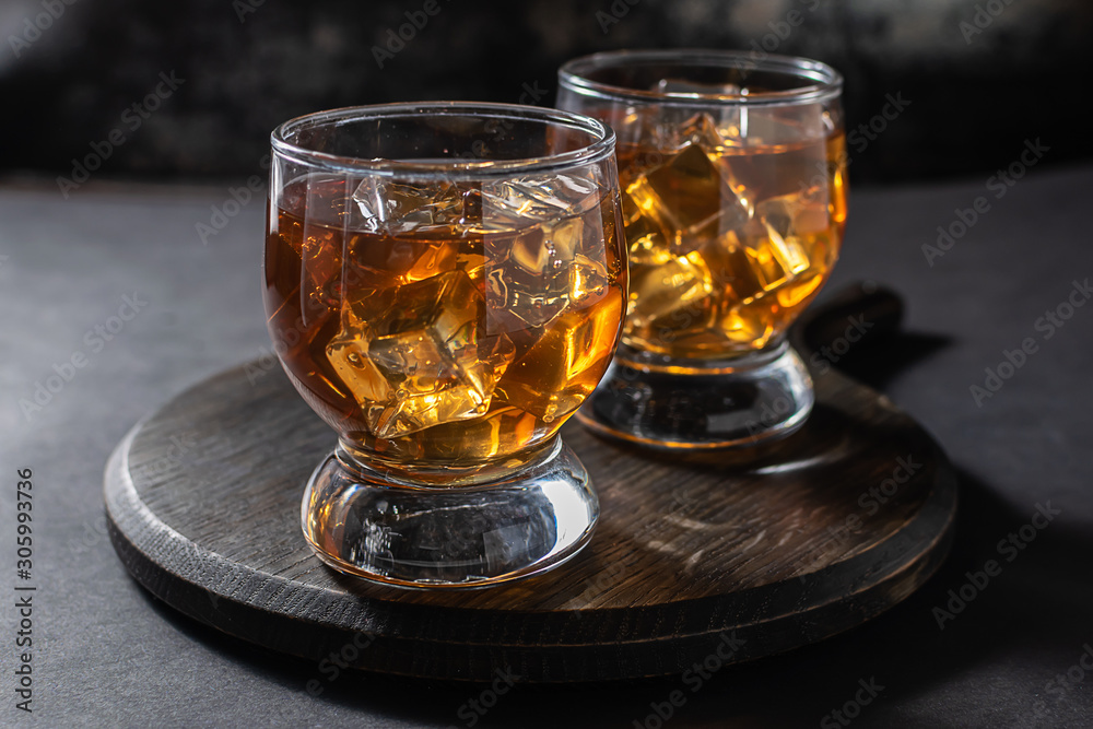 Two glasses of bourbon or rum with ice on dark background close up. Party drinks concept.