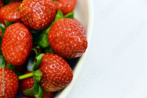 Freshly harvested red strawberries in ceramic bowl and white background.