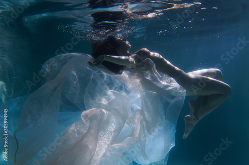 Beautiful girl swims underwater with long hair. Blue or gold background like gold. The atmosphere of a fairy tale or magic. Diving under the water with a shiny cloth