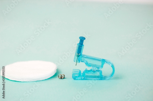 Disposable plastic gun for earrings on a turquoise background. Safe piercing