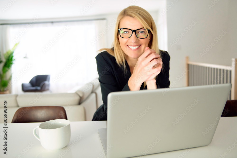 An attractive middle aged businesswoman sitting in front of laptop and managing her small business from home with coffee An attractive middle aged businesswoman sitting in front of laptop and managing her small business from home with coffee