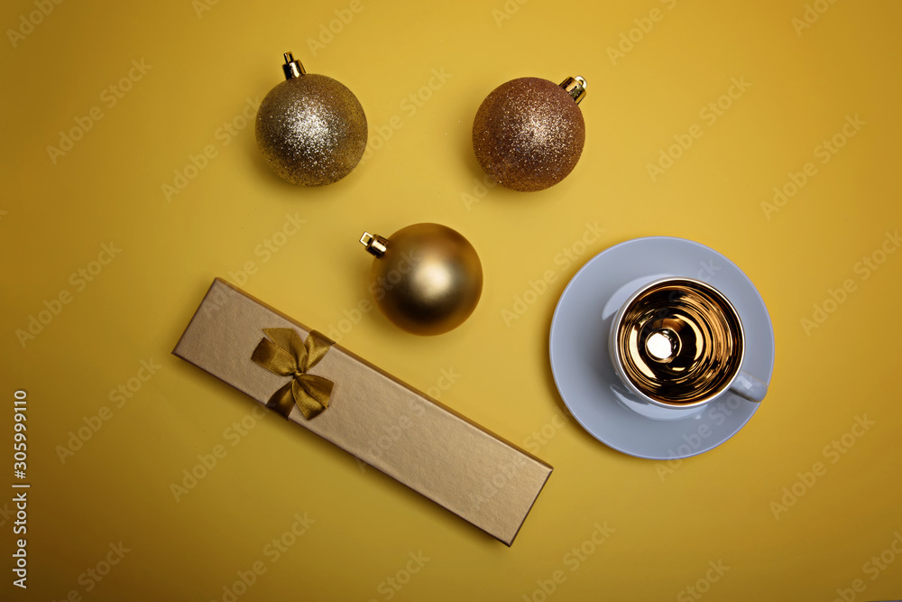 Cup of espresso coffee, golden gift box and golden Christmas balls on a yellow background. Flatlay. View from above.