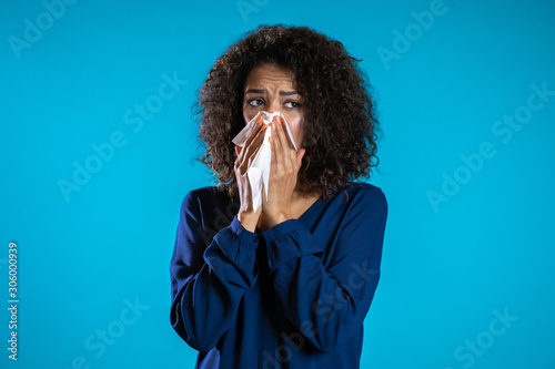 Young girl with afro hair sneezes into tissue. Isolated woman is sick, has a cold or has allergic reaction. Health, medicine, illness, treatment concept photo