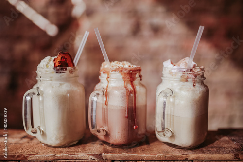 Line up of strawberry, caramel and chocolate milkshakes with marshmallows. Concept of restaurant, drinks and hospitality. Free space for text. Selective focus on the glasses.