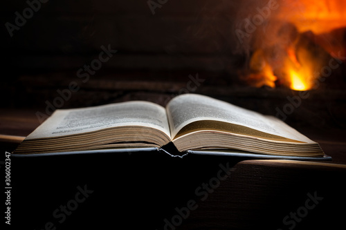 open book lies on a wooden near a burning fireplace