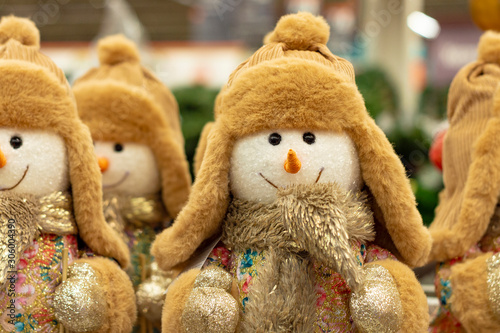 Snowmen plush toys in beige hats and fur coats are in two rows and are waiting for when they are bought for new year 2020. Front view.