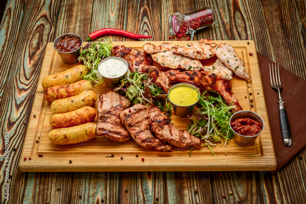 Assorted delicious grilled meat and vegetables with fresh salad and bbq sauce on cutting board on wooden background. Big set of Hot Meat Dishes