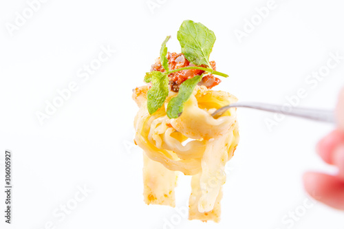 Reginette pasta with bolognese sauce decorated with parmesan and fresh herbs on a fork on a white background, held by a female hand