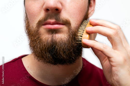 Fototapeta closeup of handsome man brushing his beard on white background isolated