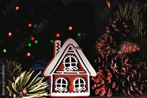 Christmas card with gingerbread house, pine branches and cones, decorations on a black background with colorful bokeh