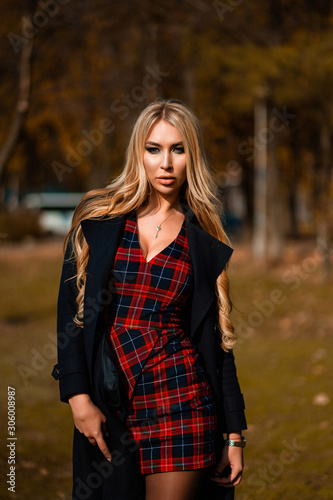 Sexy long-haired blonde in a checkered dress walks in the autumn square. Photoshoot in the autumn park