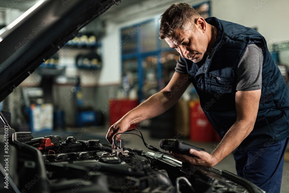 Car mechanic analyzing amperage of car battery in a repair shop. Car mechanic analyzing amperage of car battery in a repair shop.