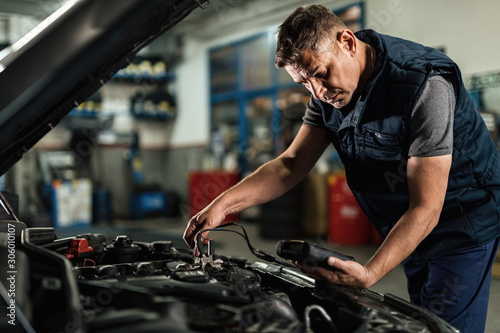 Car mechanic analyzing amperage of car battery in a repair shop.