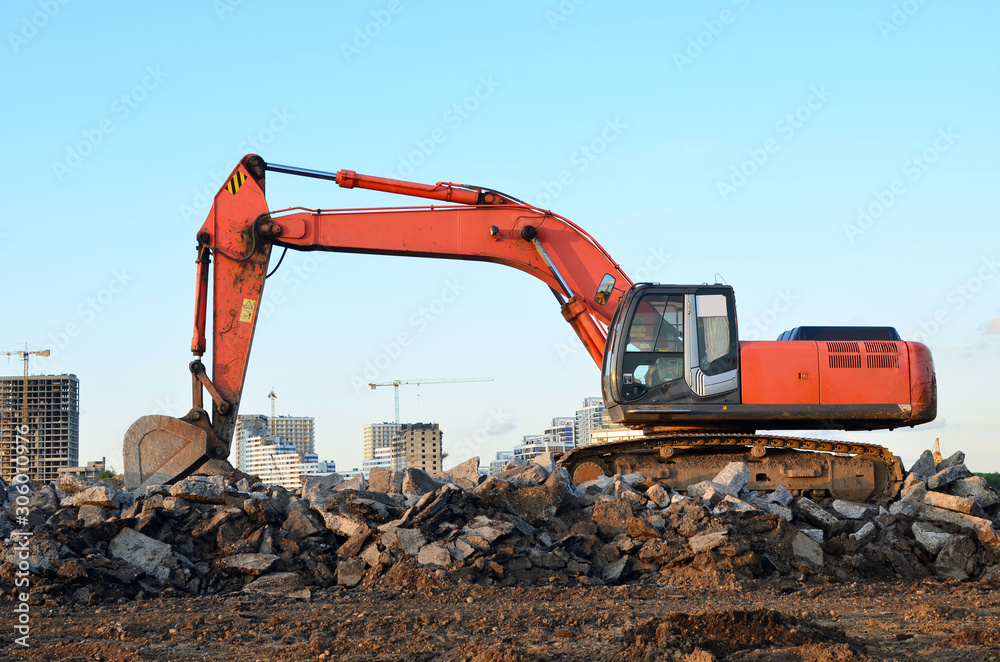 Large tracked excavator digs the ground for the foundation and construction of a new building in the city. Road repair, asphalt replacement, laying or replacement of underground sewer pipes - Image Large tracked excavator digs the ground for the foundation and construction of a new building in the city. Road repair, asphalt replacement, laying or replacement of underground sewer pipes - Image
