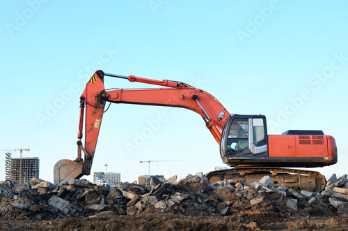 Large tracked excavator digs the ground for the foundation and construction of a new building in the city. Road repair, asphalt replacement, laying or replacement of underground sewer pipes - Image